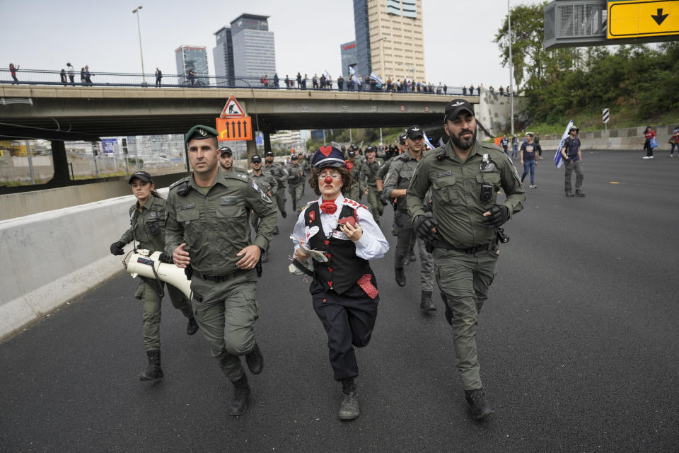 An Israeli activist dressed as a clown runs with border police as Israelis protest against plans by Prime Minister Benjamin Netanyahu's government to overhaul the judicial system block a free way in Tel Aviv, Israel, Thursday, March 23, 2023. (AP Photo/Oded Balilty)