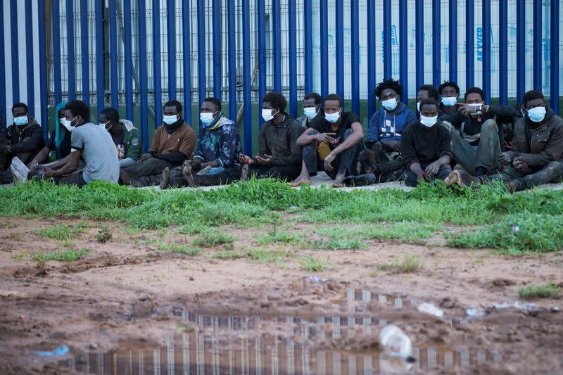 Migrants sit outside the temporary migrants center upon crossing the border fence, in Melilla