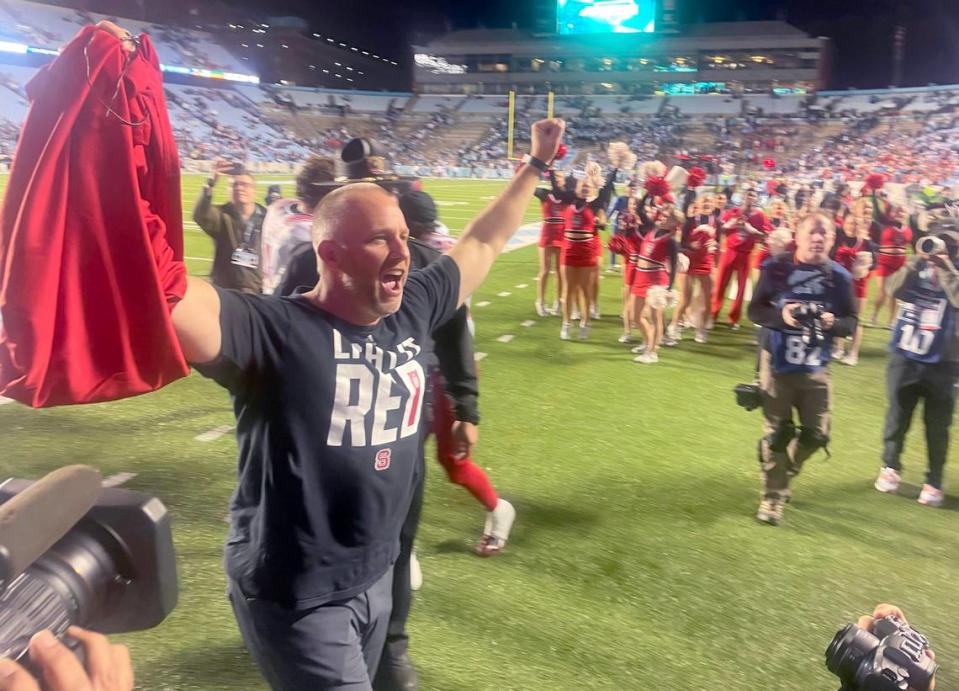 N.C. State head coach Dave Doeren celebrates by taking off a layer to show off his ‘Light it Red’ t-shirt after N.C. State’s 30-27 overtime victory over UNC at Kenan Stadium in Chapel Hill, N.C., Friday, Nov. 25, 2022.