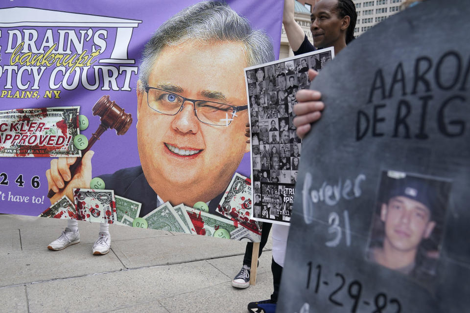 U.S. Bankruptcy Judge Robert Drain, left, is seen on a banner during a protest in front of the courthouse where the Purdue Pharma bankruptcy is taking place in White Plains, N.Y., Monday, Aug. 9, 2021. Purdue Pharma's quest to settle thousands of lawsuits over the toll of OxyContin is entering its final phase with the grudging acceptance of most of those with claims against the company. (AP Photo/Seth Wenig)