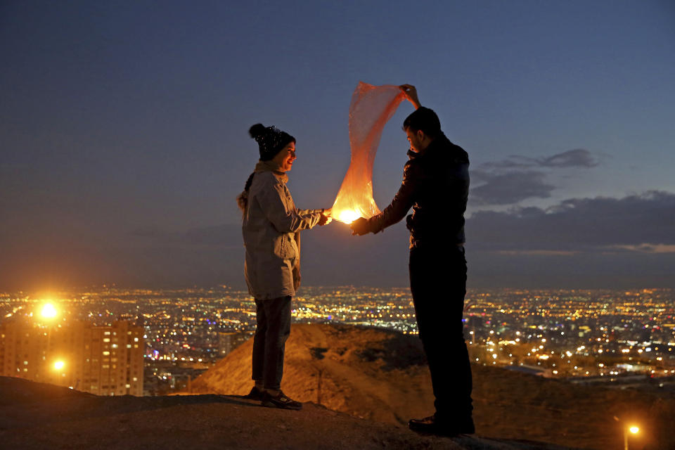 A couple lights a lantern during a celebration, known as "Chaharshanbe Souri," or Wednesday Feast, marking the eve of the last Wednesday of the solar Persian year, Tuesday, March 19, 2019, in Tehran, Iran. Iran's many woes briefly went up in smoke on Tuesday as Iranians observed a nearly 4,000-year-old Persian tradition known as the Festival of Fire. (AP Photo/Ebrahim Noroozi)