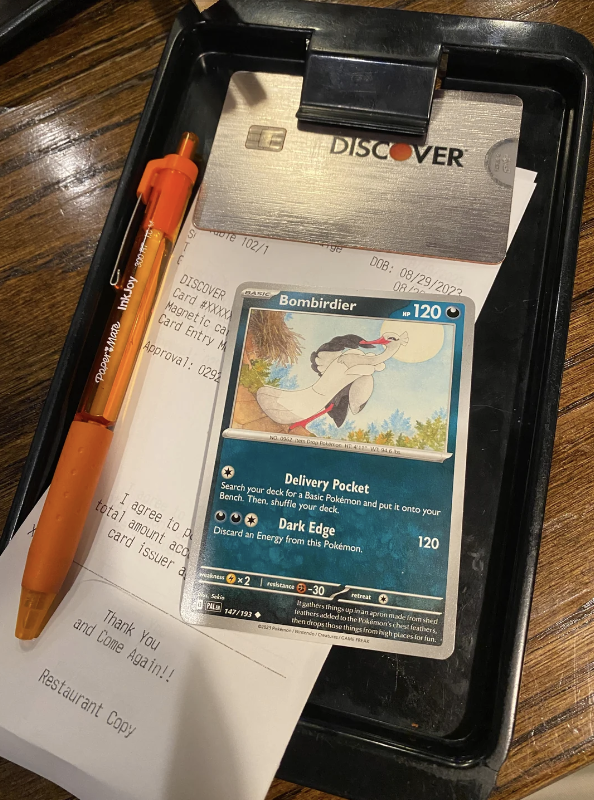 A Pokémon trading card and pens are on a restaurant bill holder