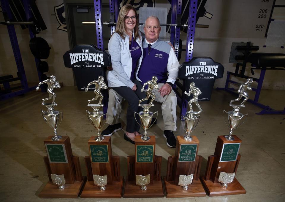 Central football coach Jay Sharrett poses for a photo with his wife, Lynda, and trophies from the Tigers' appearances in the state finals. Sharrett has announced his retirement after leading the program for 20 seasons. His wife put together the team program throughout his tenure as coach.