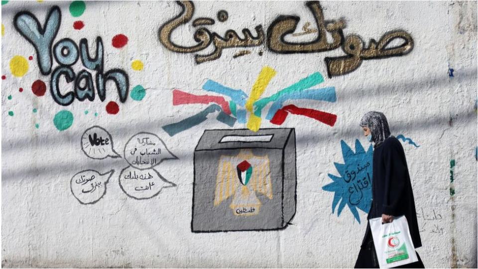 Una mujer camina frente a un mural con publicidad electoral en la Ciudad de Gaza, abril 2021