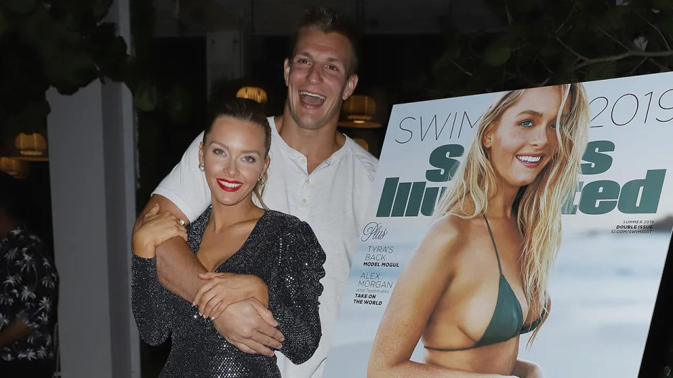 Gronk embracing Camille Kostek next to her SI cover.