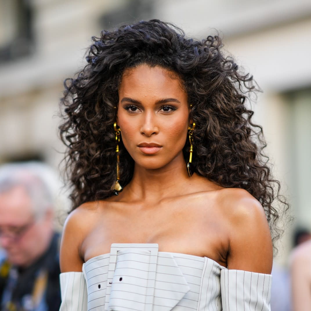  Cindy Bruna wears gold long pendant earrings, a white gray with small black striped print pattern shoulder-off / large belted / long sleeves corset jacket from Jean-Paul Gaultier, matching white gray with small black striped print pattern wide legs suit pants, outside Jean-Paul Gaultier, during Paris Fashion Week - Haute Couture Fall Winter 2022 2023, on July 06, 2022 in Paris, France. 