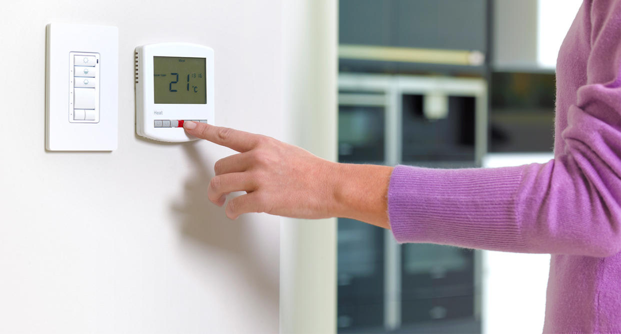 Woman setting thermostat temperature at home. (Getty Images)