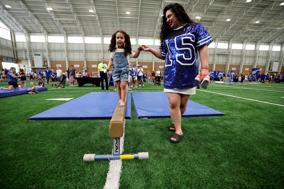 Delilah Mendieta, with the help of her mom Scarlett Mendieta, walks on the balance beam inside the Indoor Practice Facility as BYU holds a party to celebrate their move into the Big 12 Conference with music, games and sports exhibits in Provo on Saturday, July 1, 2023. | Scott G Winterton, Deseret News