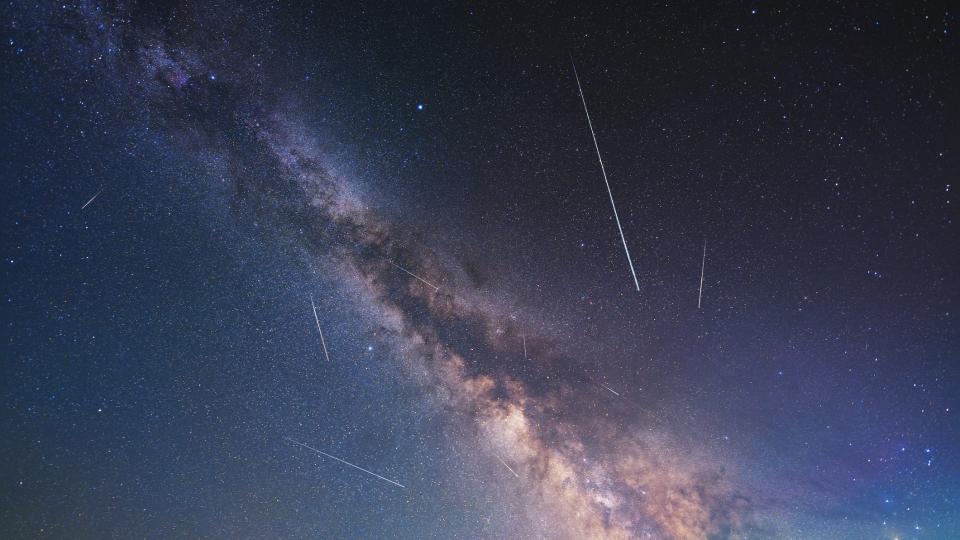 Meteor shower trails appear as long, white streaks of light against a background of the Milky Way.