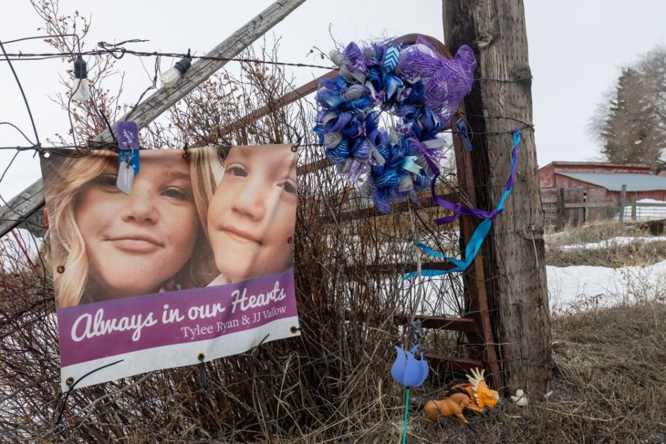 a picture of tylee ryan and j j vallow on a fence in a makeshift memorial, with flowers, ribbons, and the words always in our hearts