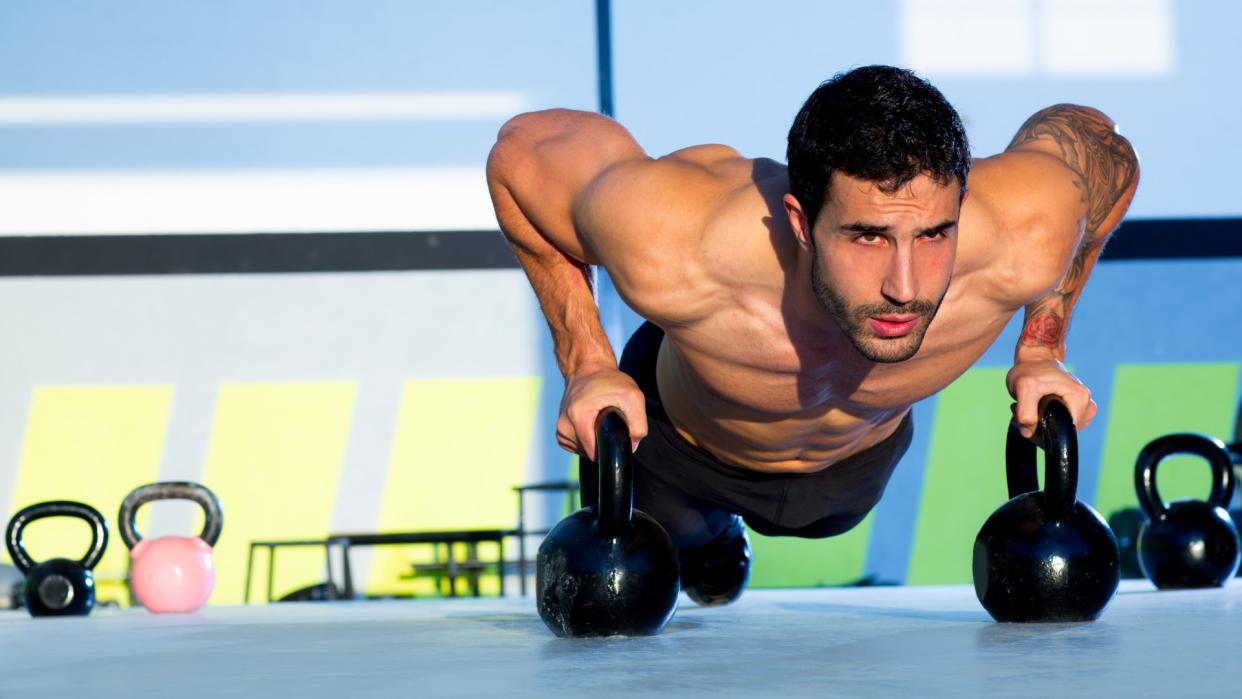  Man performing a push-up with two kettlebells during outdoor workout. 