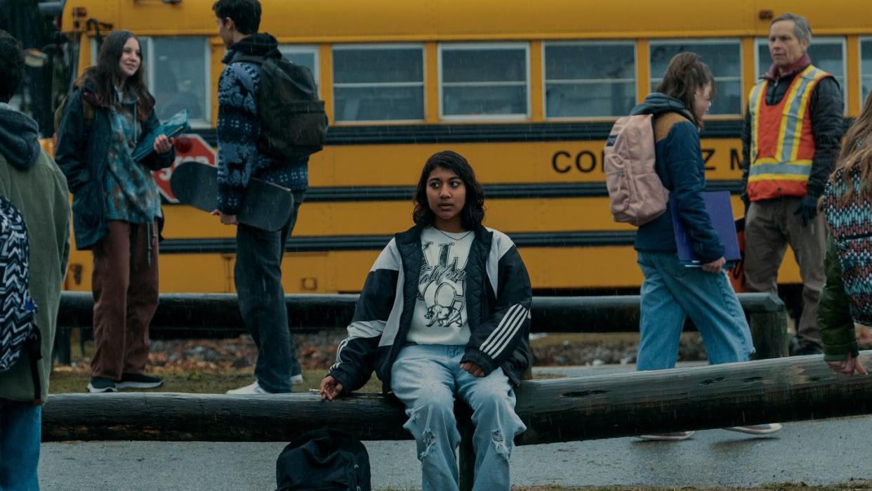 a person sitting on a bench in front of a yellow school bus