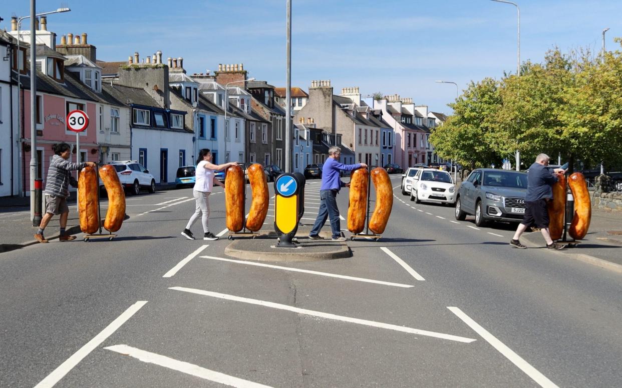An image from Shiro Masuyama's Brexit Sausage exhibition, depicting eight giant sausages being chaperoned across the road - News Scan