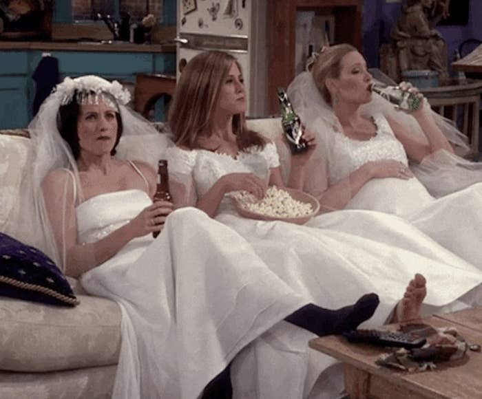 Monica, Rachel, and Phoebe drinking and sitting on the couch in wedding dresses