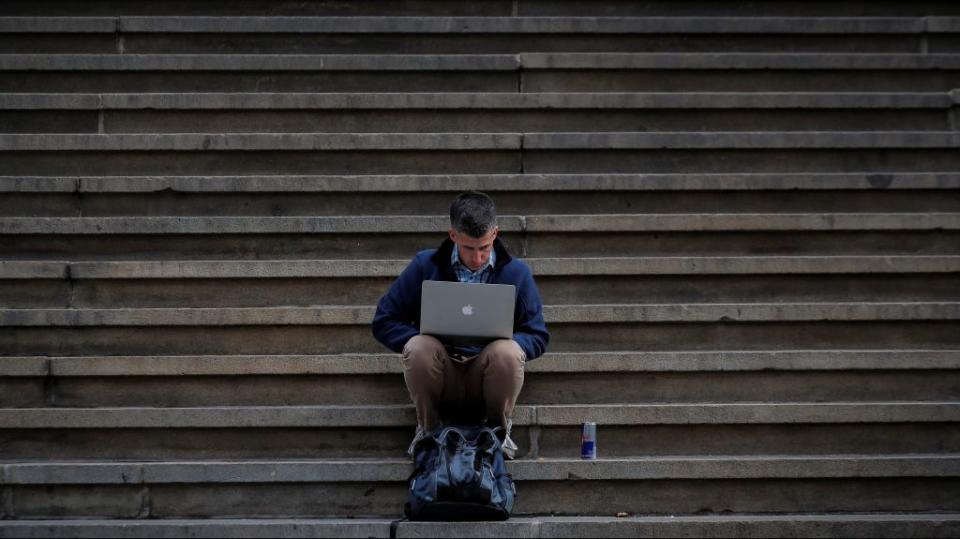 A man uses his Apple laptop on the steps of Federal Hall on Wall St. in the financial district of New York