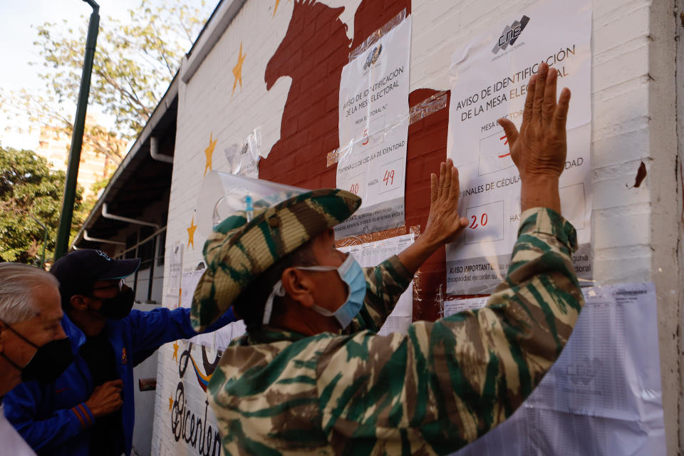 A government militia posts a polling station information poster during regional elections, in the San Agustin neighborhood of Caracas, Venezuela, Sunday, Nov. 21, 2021. Venezuelans go to the polls to elect state governors and other local officials. (AP Photo/Jesus Vargas)