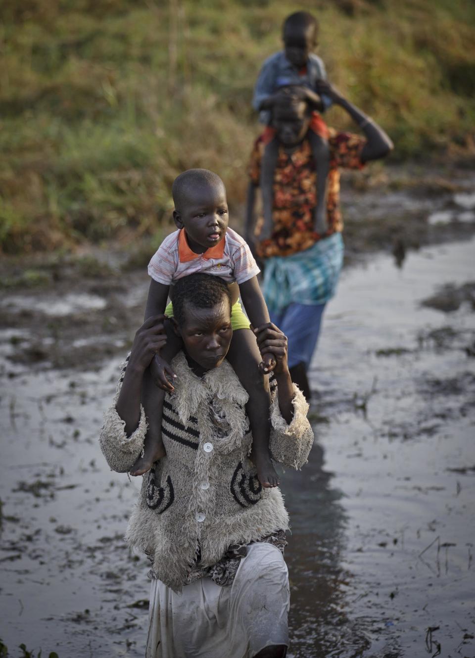 Displaced people wade through mud as they get off a river barge from Bor, some of the thousands who fled the recent fighting between government and rebel forces in Bor by boat across the White Nile, in the town of Awerial, South Sudan Thursday, Jan. 2, 2014. The international Red Cross said Wednesday that the road from Bor to the nearby Awerial area "is lined with thousands of people" waiting for boats so they could cross the Nile River and that the gathering of displaced is "is the largest single identified concentration of displaced people in the country so far". (AP Photo/Ben Curtis)