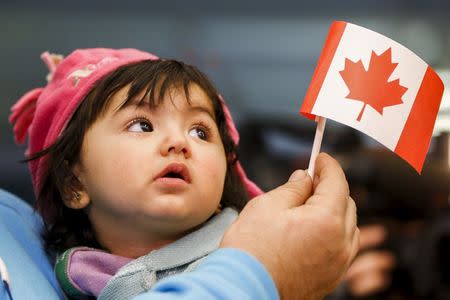 A young Syrian refugee looks up as her father holds her and a Canadian flag at the as they arrive at Pearson Toronto International Airport in Mississauga, Ontario, December 18, 2015. REUTERS/Mark Blinch