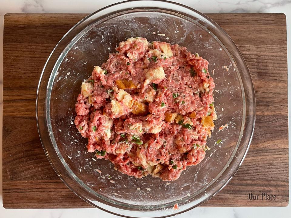 Meat, bread, and other ingredients mixed in a glass bowl.