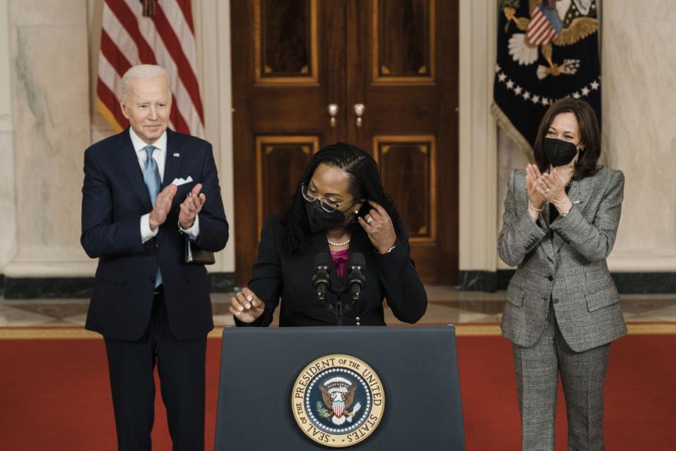 Ketanji Brown Jackson speaks at a lectern, flanked by President Biden and Vice President Kamala Harris.