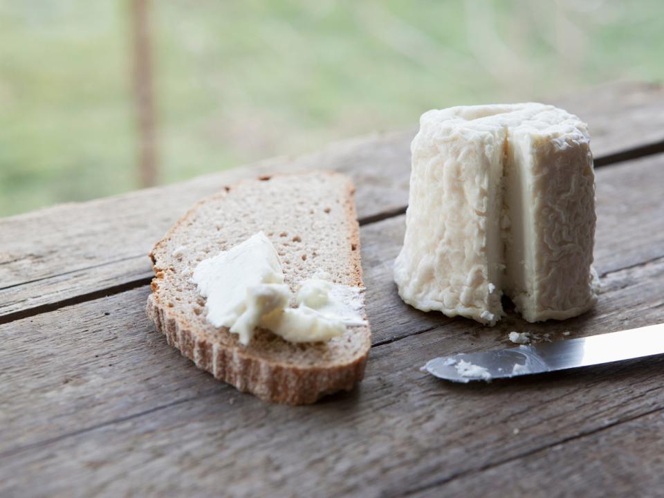 A small wheel of soft cheese with a slice cut out and spread onto a piece of bread