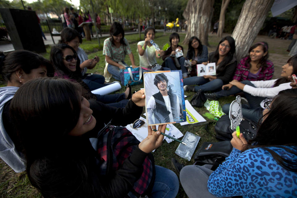 In this May 11, 2013 photo, a fan of South Korean singer Hyun Joong shows her picture of him as she sits with other fans as they celebrate the singer's birthday in Ramon Castilla park in Lima, Peru. Hundreds of fans of K-pop gather each week in the downtown park to dance to the energetic music. Some dress up as Korean comic book characters. (AP Photo/Martin Mejia)