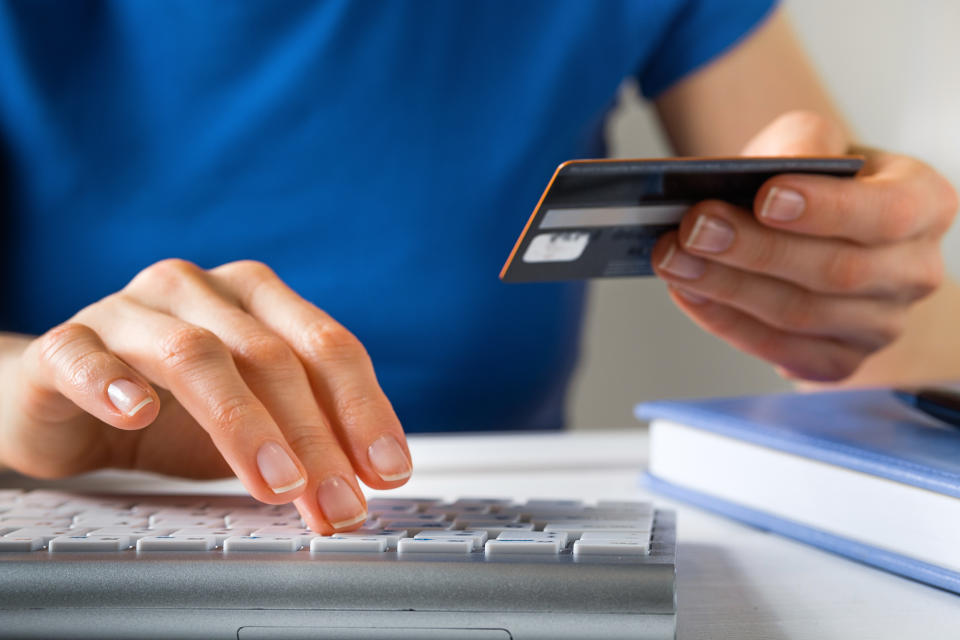 A Woman Is Holding A Credit Card, Typing on A Laptop Keyboard. There's a Notepad and a Pen next to it. The Concept of Buying Online, Ordering Products at Home, and paying via the Internet.