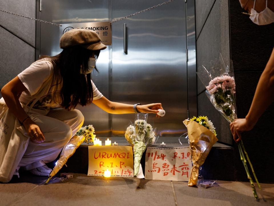 masked people leave flowers and candles at a memorial on the sidewalk