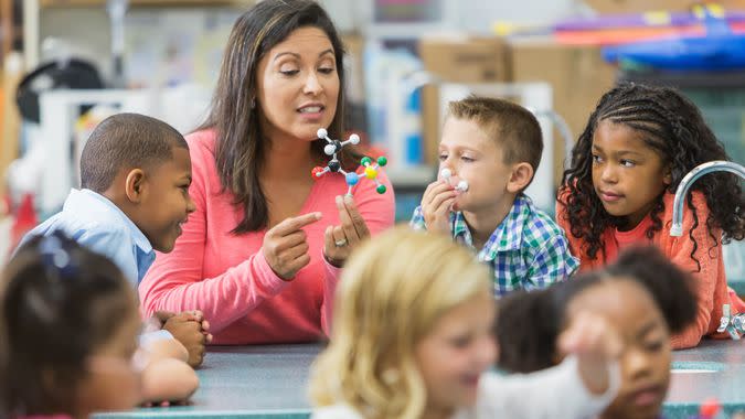 An Hispanic woman in her 40s teaching a multi-ethnic group of elementary school students in science lab.