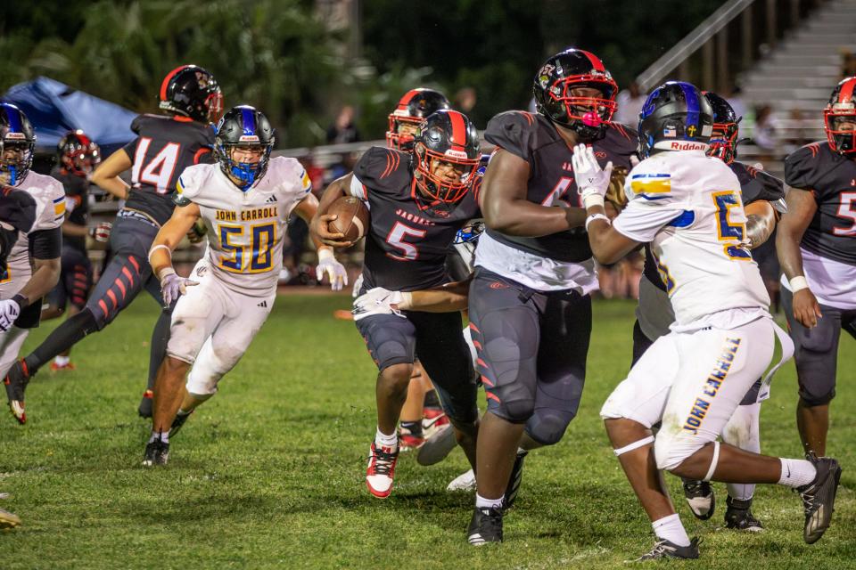 Terrell Harmon (5) de Port St. Lucie lleva el balón a través del tráfico en un partido de fútbol americano de la escuela secundaria contra John Carroll Catholic el jueves 12 de septiembre de 2024 en Port St. Lucie. Los Rams ganaron 49-0.