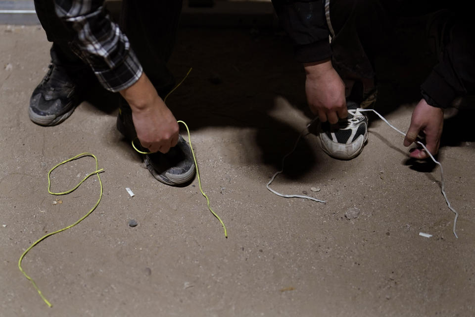 Dos hombres retiran los cordones de sus zapatillas mientras esperan para solicitar asilo tras cruzar al frontera desde México, el 11 de julio de 2023, cerca de Yuma, Arizona. El repunte en la inmigración ha sido posible por el descubrimiento este año de una nueva a través de Nicaragua, donde la laxitud de los requisitos de entrada permite a los mauritanos y a otros extranjeros adquirir una visa de bajo costo sin necesidad de demostrar que van a continuar su viaje. (AP Foto/Gregory Bull)