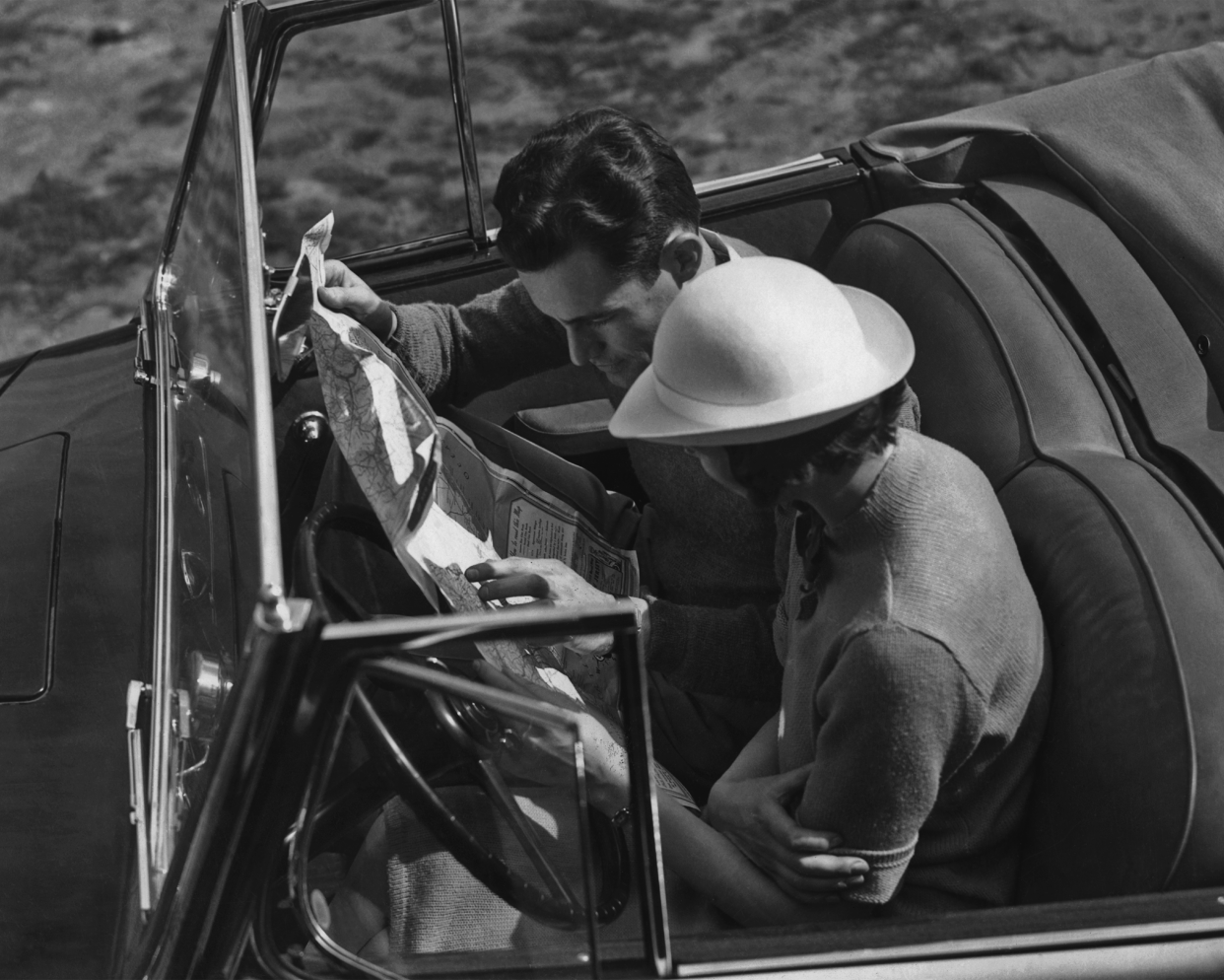 A couple checking a road map in a convertible car circa 1950.