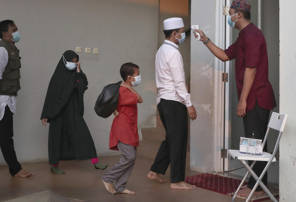 An official takes the body temperature reading of worshippers arriving for an Eid al-Adha prayer as to curb the spread of coronavirus during an Eid al-Adha prayer at Zona Madina mosque in Bogor, Indonesia, Tuesday, July 20, 2021. Muslims across Indonesia marked a grim Eid al-Adha festival for a second year Tuesday as the country struggles to cope with a devastating new wave of coronavirus cases and the government has banned large gatherings and toughened travel restrictions. (AP Photo/Tatan Syuflana)