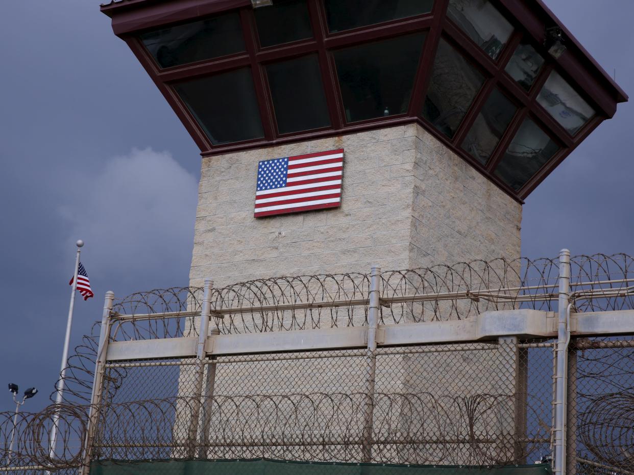 A guard watchtower with a print of the American flag behind a barbed-wire fence.