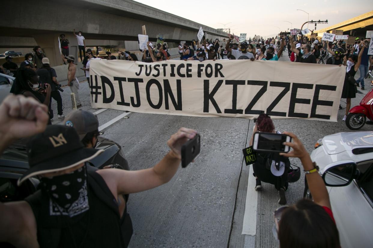 People on the freeway protest, holding a "Justice for #Dijon Kizzee" banner and shooting photos and film.