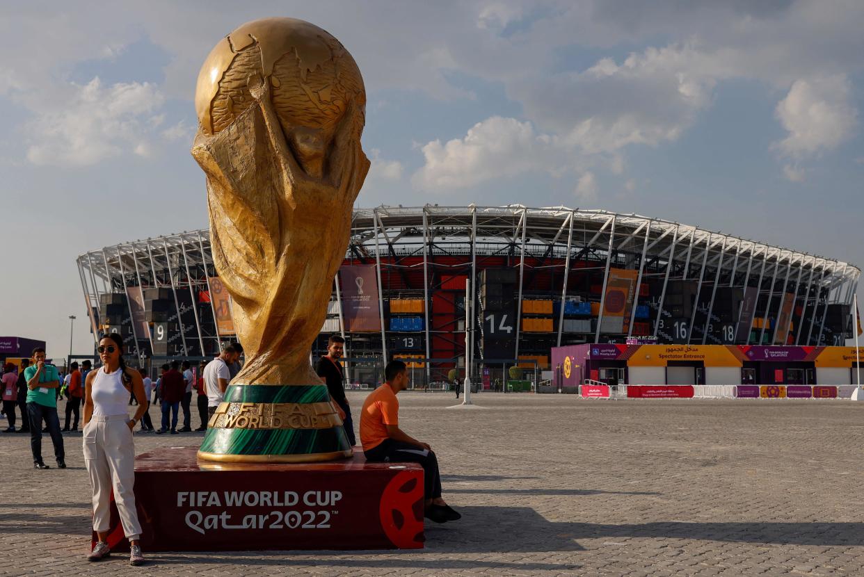 People pose for photos next to a giant replica on the World Cup trophy in front of Stadium 974 on November 18, 2022 in Doha, Qatar, ahead of the Qatar 2022 World Cup football tournament. (Photo by David GANNON / AFP) (Photo by DAVID GANNON/AFP via Getty Images)