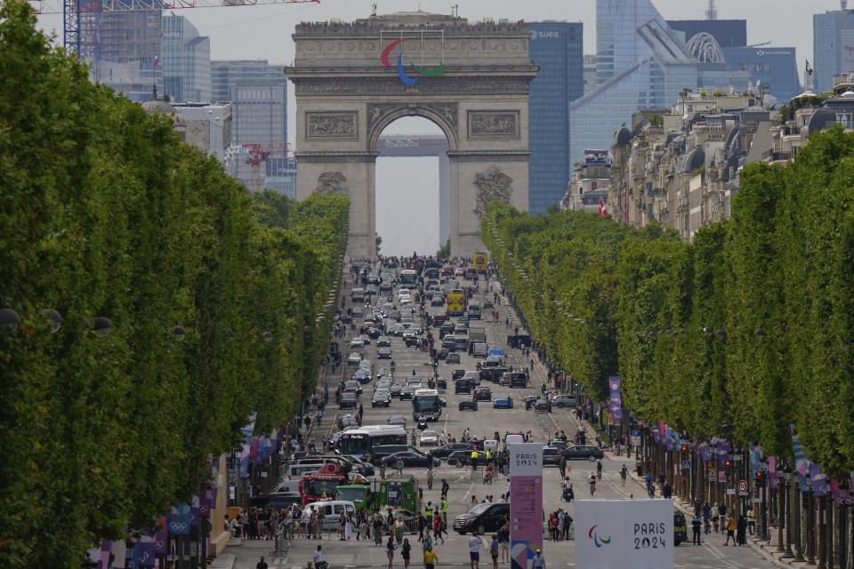 Peatones y vehículos circulan por la avenida Champs Elysees, con el Arco del Triunfo de fondo, en la previa a la inauguración de los Juegos Olímpicos de París, jueves 25 de julio, 2024. (AP Foto/Frank Franklin II)