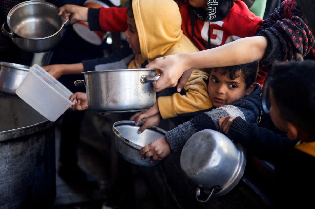 Palestinian children wait to receive food cooked by a charity kitchen amid shortages of supplies in Rafah (Mohammed Salem/Reuters)