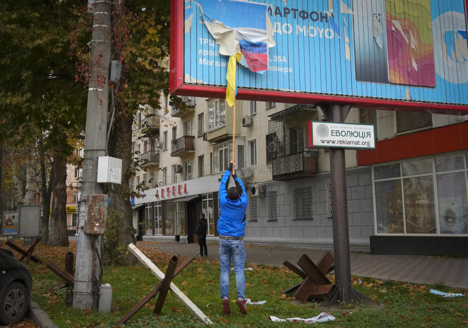 A local resident removes the Russian flag from a billboard in central Kherson, Ukraine, Sunday, Nov. 13, 2022. The Russian retreat from Kherson marked a triumphant milestone in Ukraine's pushback against Moscow's invasion almost nine months ago. (AP Photo/Efrem Lukatsky)