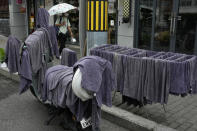 A resident walks by towels hung up to dry on a scooter and a drying rack outside a barber shop in Beijing, Monday, Aug. 15, 2022. China’s central bank trimmed a key interest rate Monday to shore up sagging economic growth at a politically sensitive time when President Xi Jinping is believed to be trying to extend his hold on power. (AP Photo/Ng Han Guan)