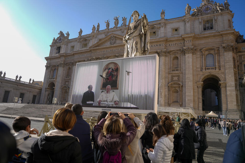 Pope Francis appears on a giant monitor set up in St. Peter's Square at The Vatican, Sunday, Dec. 3, 2023, as he blesses the faithful gathered in the square for the traditional Angelus noon prayer. Francis skipped his weekly Sunday appearance at a window because suffering from a mild flu. (AP Photo/Andrew Medichini)