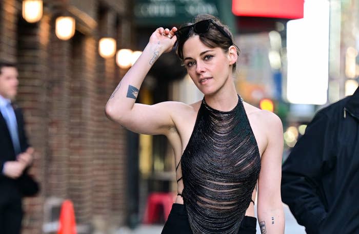 Kristen Stewart in a sleeveless mesh dress, walking outdoors with sunglasses on her head