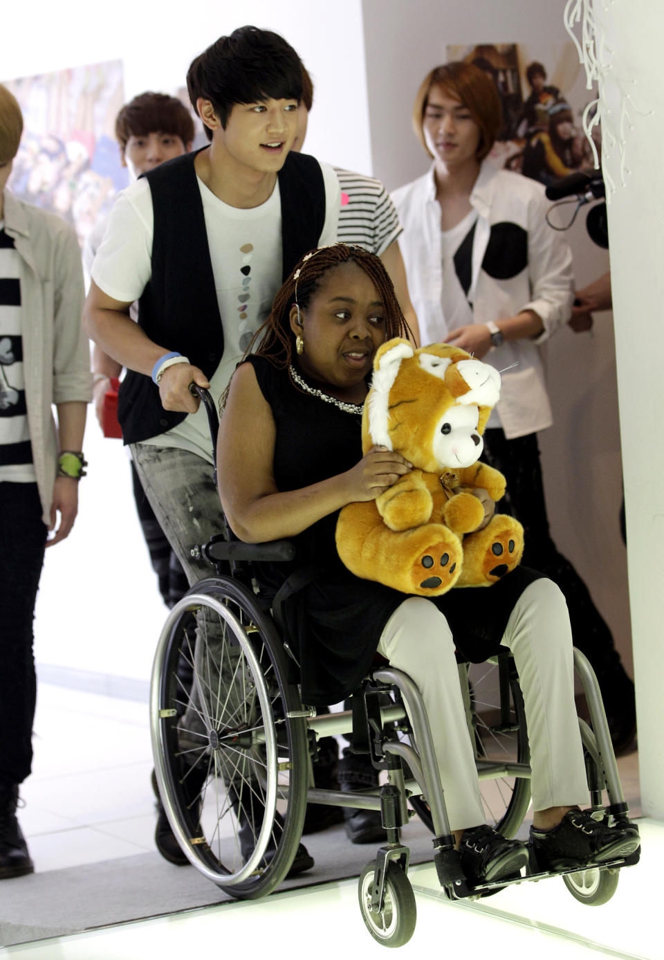 Donika Sterling from New York, in a wheelchair, gets help from Minho, a member of SHINee, on her arrival for meeting with the South Korean pop group in Seoul, South Korea, Wednesday, June 20, 2012. The 15 year-old American K-pop fan, who is suffering a disease that gradually causes loss of muscle tissue and slows down parts of the body, met and sang with the boy band she idolizes. (AP Photo/Lee Jin-man)