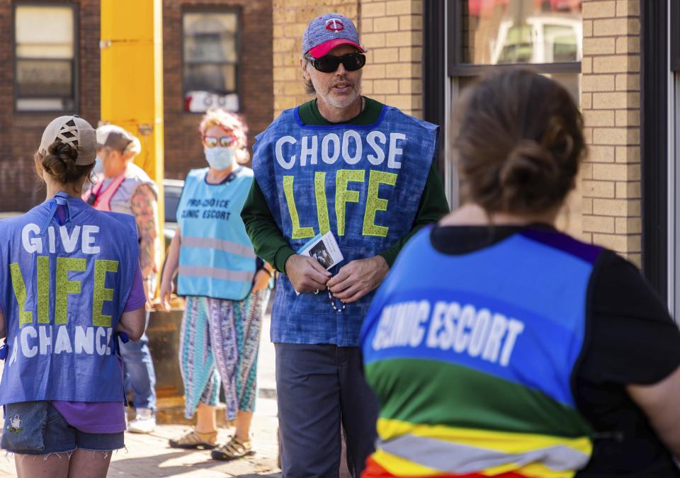 Anti-abortion protester Jeff Asmussen, center, attempts to talk to a clinic escort, Thursday, July 7, 2022, at WE Health Clinic in Duluth, Minn. Protesters like Asmussen are often seen outside the clinic during days when abortions are taking place. "I want to be a witness to the dignity of human life," Asmussen said. "We're rallying the troops out here and offering women going in there a true choice." (AP Photo/Derek Montgomery)