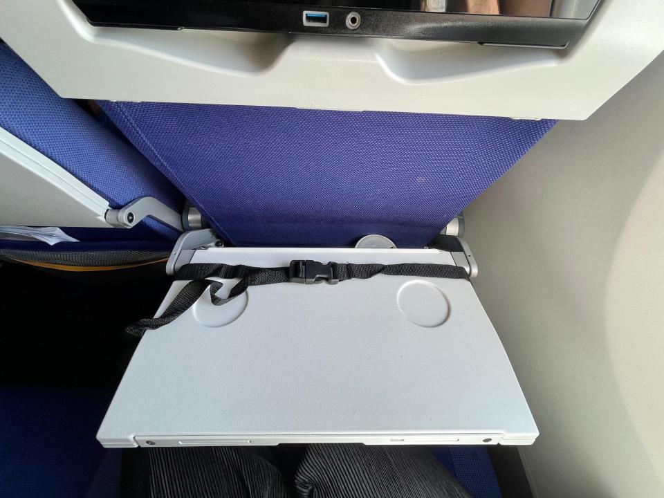 A black strap looped around an open airplane tray table.