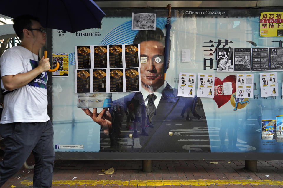 In this Sept. 15, 2019, photo, a man holding an umbrella walks by a bus stop advertisement filled with protest art posters. As Hong Kong enters its fourth month of steady protests, the city is embracing for another violent weekend prior to the upcoming 70th National Day on Oct. 1. (AP Photo/ Vincent Yu)