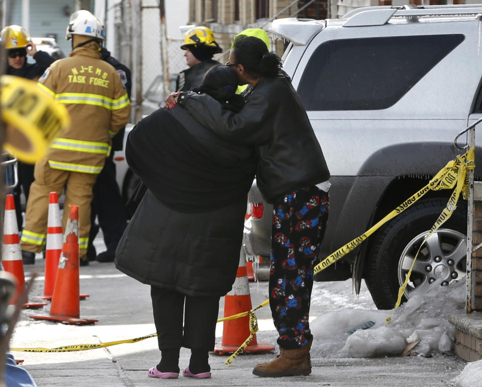 A woman is consoled by another woman near the scene of a four-alarm fire in Jersey City, N.J. on Thursday, March 6, 2014. Mayor Steven Fulop said a couple in their 80s and their two sons, who are in their 50s, were unaccounted for after the blaze on Grant Avenue was extinguished early Thursday. Authorities have not identified the two bodies that were found in the charred home. (AP Photo/Julio Cortez)