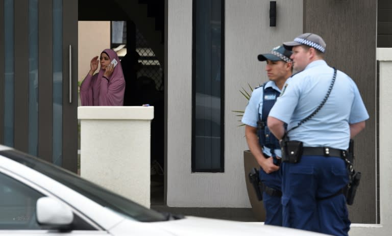 A resident of a house talks on a phone while New South Wales police officers stand guard in Sydney, on October 7, 2015