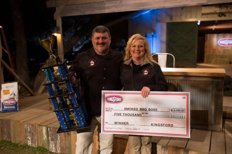 Robby and Stephanie Royal of the award-winning BBQ team Rescue Smokers stand with a trophy and check after winning a Kingsford sponsored competition.
