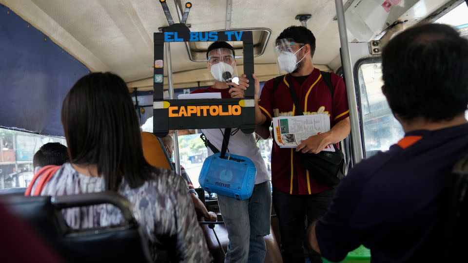 Juan Pablo Lares, right, holds a cardboard frame in front of his associate Maximiliano Bruzual who reads their newscast "El Bus TV Capitolio" to commuters on a bus in Caracas, Venezuela, Saturday, July 31, 2021. - Ariana Cubillos/AP